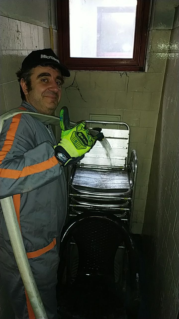 The Poltro in coveralls and work gloves, blasting a stack of chairs with a fire hose in a very dirty room